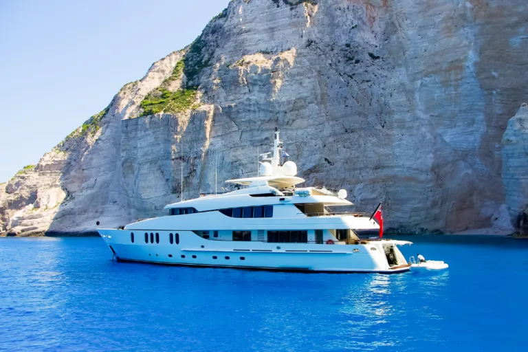 Yacht anchors in blue water with mountain in the back