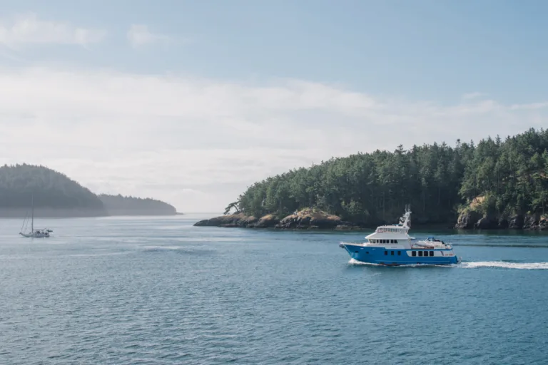 Yacht driving through blue water with mountains in the back